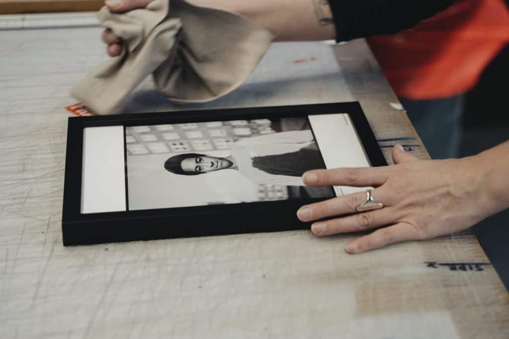 Person cleaning a framed art print representing high-quality handmade framing and careful finishing before eco-friendly packaging.